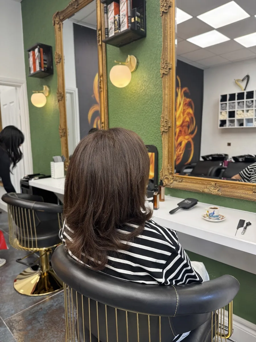 A finished glossy brown blow-dry seen from behind in the styling chair, gold mirror and green wall beyond